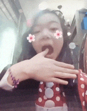 a girl wearing a red and white polka dot shirt has a flower on her face