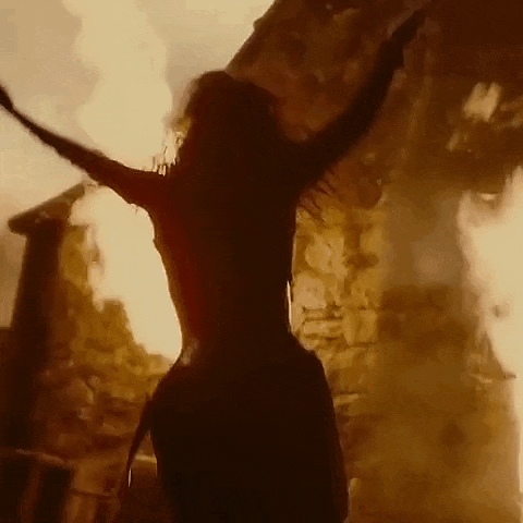 a woman is standing in front of a building on fire with her arms outstretched .