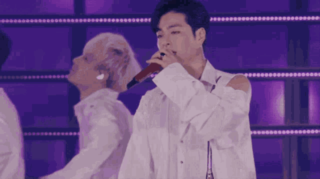 a man in a white shirt singing into a microphone with a purple background