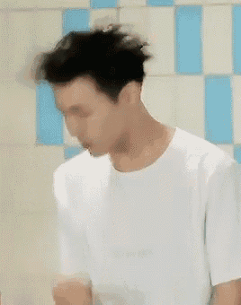 a man in a white shirt is brushing his teeth in front of a tiled wall .