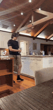 a man is standing in a kitchen holding a remote control while a tiktok video is being played