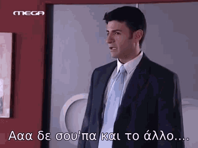 a man in a suit and tie is standing in front of a wall with greek writing on it .