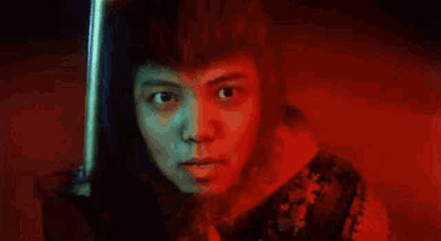 a close up of a person holding a sword in a dark room with red lights .