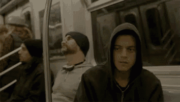 a man in a hooded jacket is sitting on a subway train with other people .