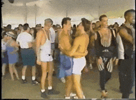 a group of people are dancing in a tent and one of the men is kissing another man