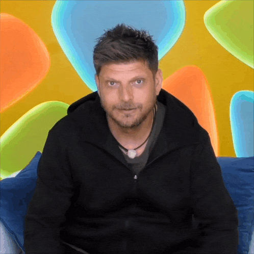 a man in a black jacket is sitting in front of a colorful background of balloons