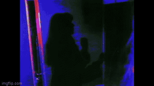 a woman is standing in front of a mirror in a dark room with a blue light behind her .