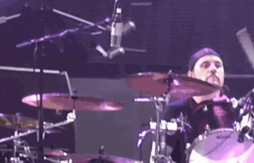 a man is playing drums in front of a microphone with a purple background