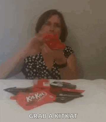 a woman is sitting at a table taking a picture of a kit kat bar .