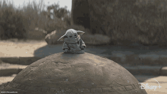 a baby yoda sits on top of a large rock with a disney logo in the background