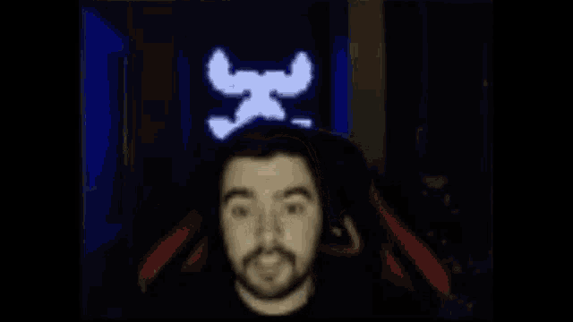 a man with a beard is saluting in front of a screen that says skull and crossbones .