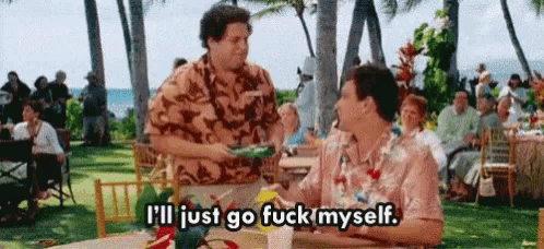 a man in a hawaiian shirt is sitting at a table talking to another man while a crowd watches .