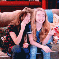 two girls are sitting on a couch and smiling for the camera
