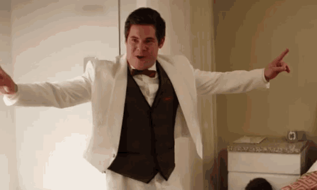 a man in a white tuxedo and black vest is pointing at something