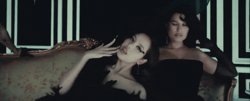 two women are sitting on a couch and one has a hand on her face