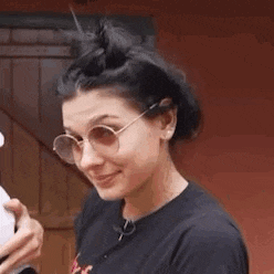 a woman wearing glasses and a bun is smiling and waving .