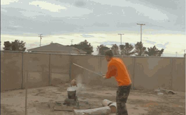 a man in an orange shirt is holding a sword in a yard