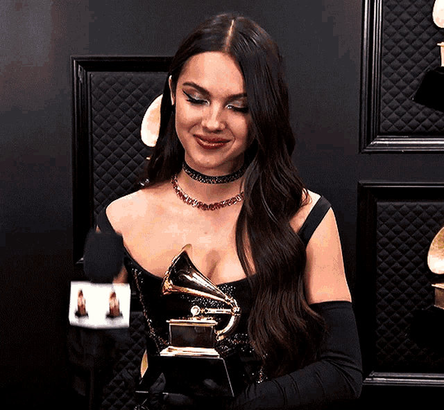 a woman in a black dress is holding a grammy