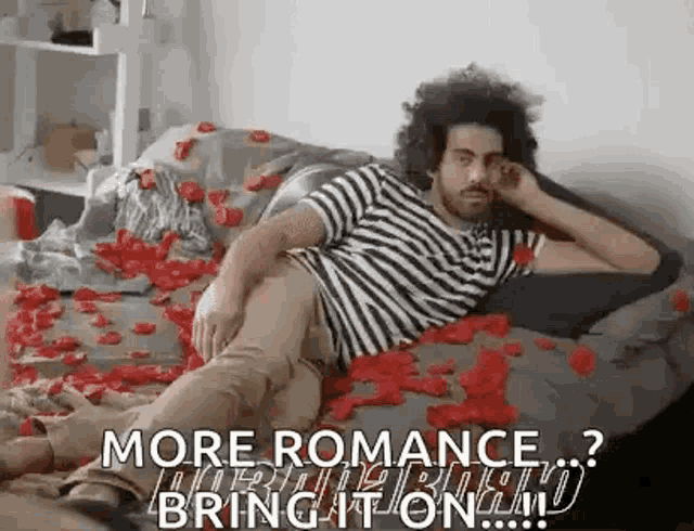 a man is laying on a bed covered in rose petals and talking on a cell phone .