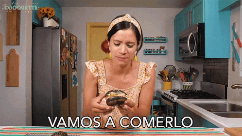 a woman in a kitchen is holding a donut and says vamos a comerlo