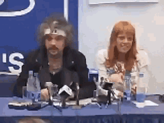 a man and a woman are sitting at a table with bottles and a sign that says ' s ' on it
