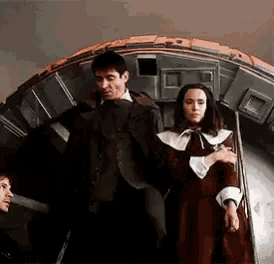 a man in a suit and a woman in a red dress are standing next to each other in front of a large object .