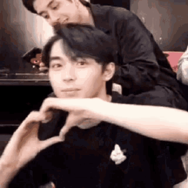 a man is making a heart shape with his hands on his face .