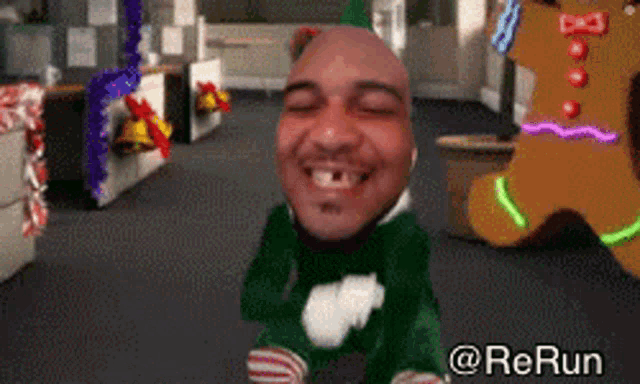 a man in an elf costume is smiling in front of a gingerbread man in an office