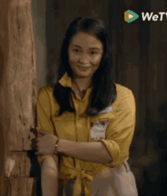 a woman in a yellow shirt is leaning against a tree trunk .