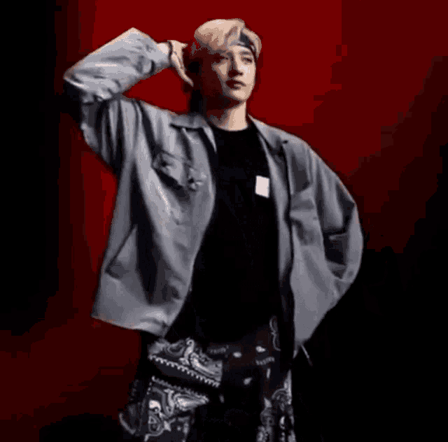 a young man is standing in front of a red background wearing a bandana and a jacket .