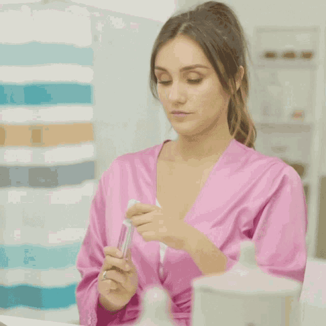 a woman in a pink robe is holding a toothbrush in front of a mirror