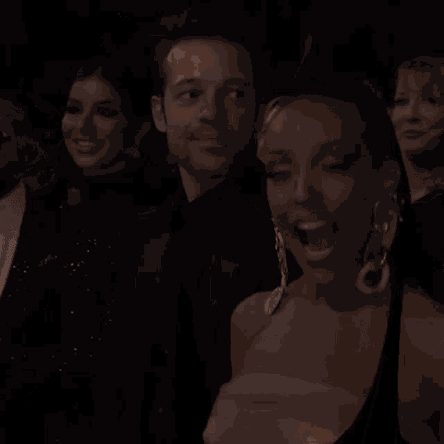 a group of people are sitting in a dark room and one of them is smiling