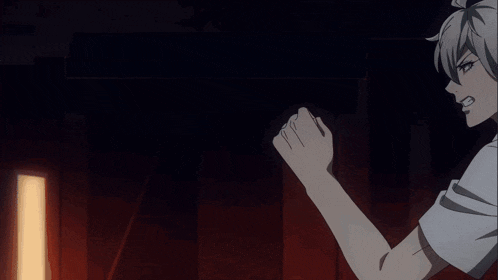 a man in a white shirt is holding his fist up in a dark room