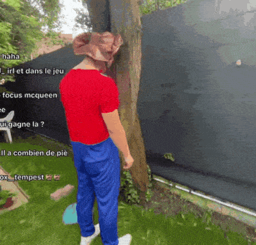 a man in a red shirt and blue pants is standing next to a tree in a garden