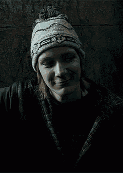 a man wearing a knitted hat and a black jacket is smiling in the dark .
