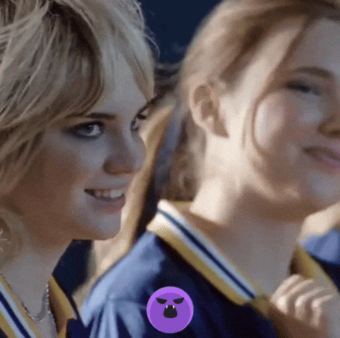 two girls are standing next to each other and one has a purple circle with a smiley face on it .