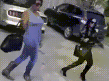 a woman in a blue top is walking down a street next to a car .