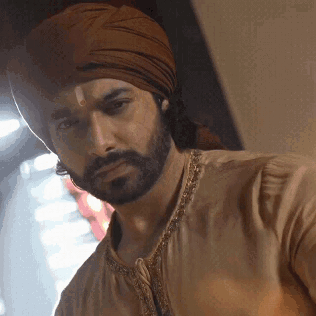a man with a beard and a turban on his head looks at the camera
