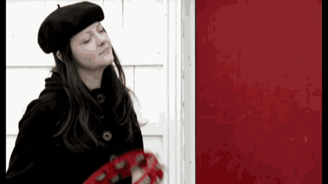 a woman in a black beret holds a red tambourine in front of a red door