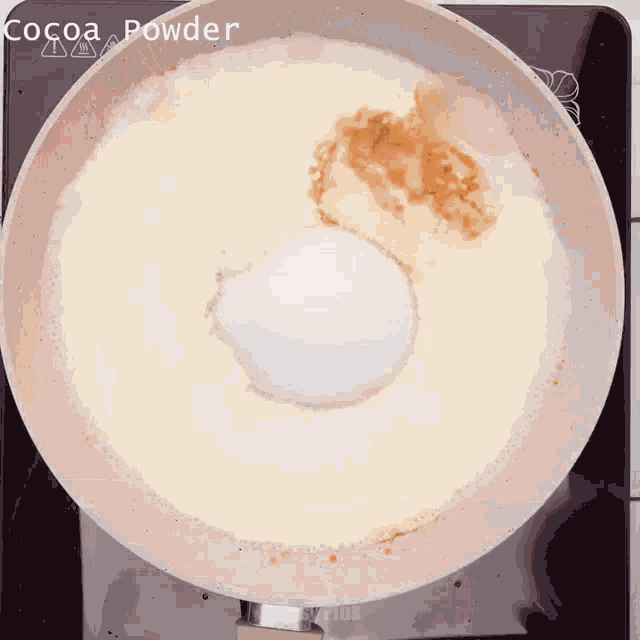 cocoa powder is being poured into a pan of milk