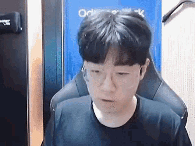 a young man wearing glasses and a black shirt is sitting in a gaming chair .
