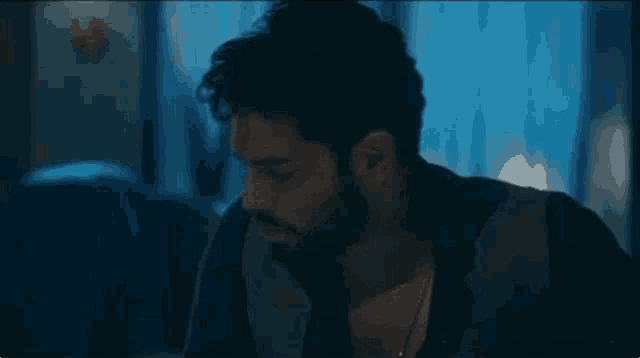 a man with a beard is sitting in a dark room with his eyes closed .