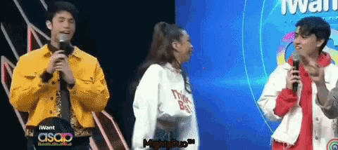 a man in a yellow jacket is speaking into a microphone while a woman in a white sweater stands behind him