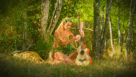a naked man playing a guitar in a forest