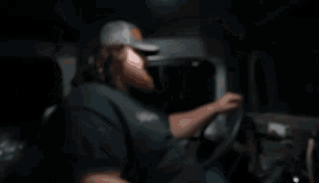 a man with a beard wearing a nike hat is driving a car