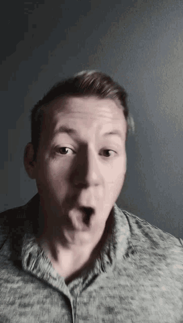 a man in a grey shirt making a surprised face
