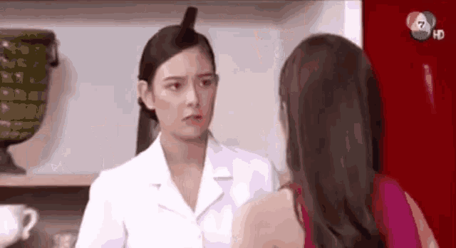 a woman in a white coat is talking to another woman in a kitchen .