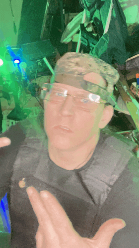 a man wearing glasses and a camouflage hat is giving the middle finger