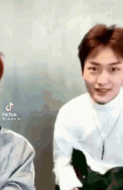 a young man wearing a white turtleneck sweater and a necklace is standing next to another man .