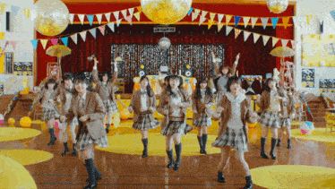 a group of girls in school uniforms are dancing in a room with balloons and flags